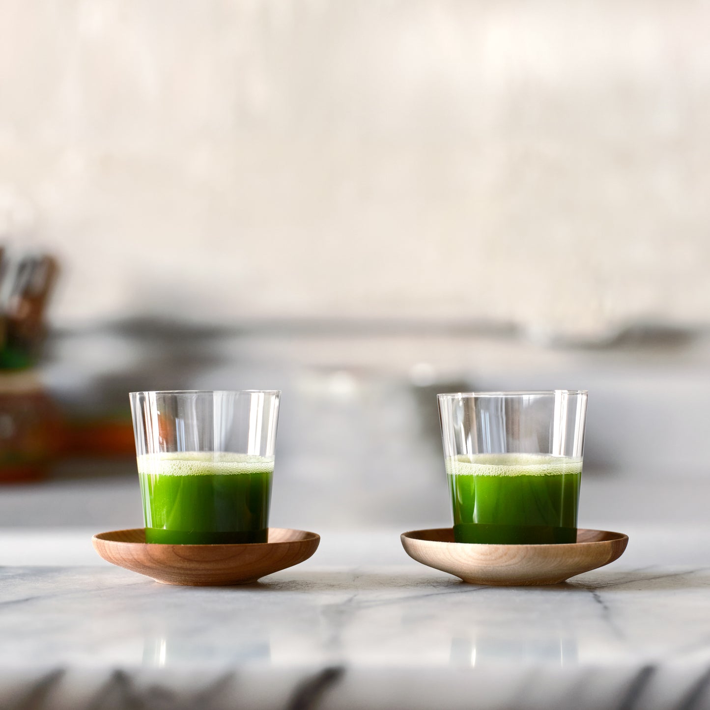 Two sets of Matcha Shot Glasses and Wooden Saucers sit next to each other, full of bright green matcha shots.