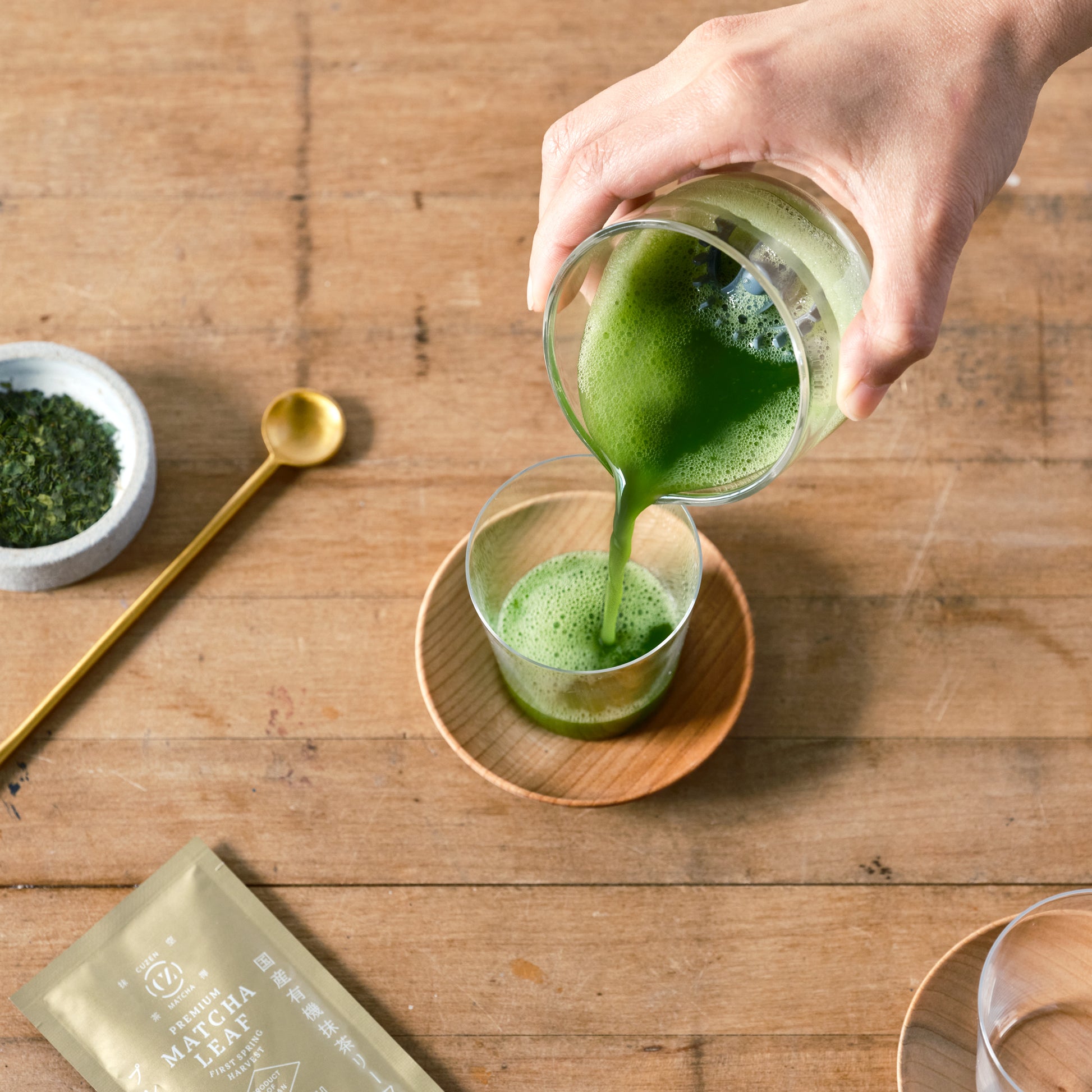 A shot of bright green matcha is poured from the whisking cup into our Matcha Shot Glass, which is set on a Wooden Saucer.