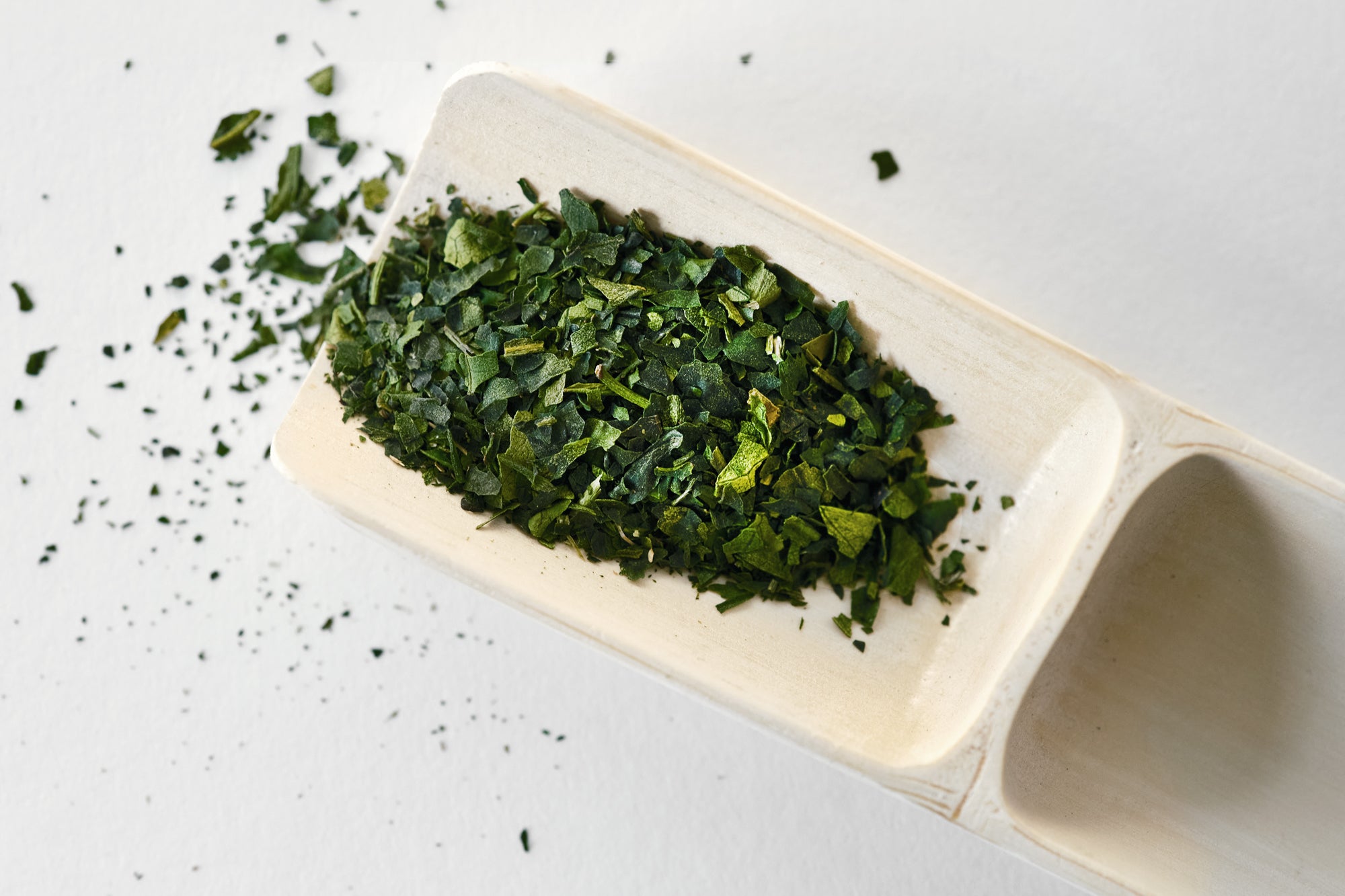 A larger bamboo scoop holding dark green, whole matcha leaves.