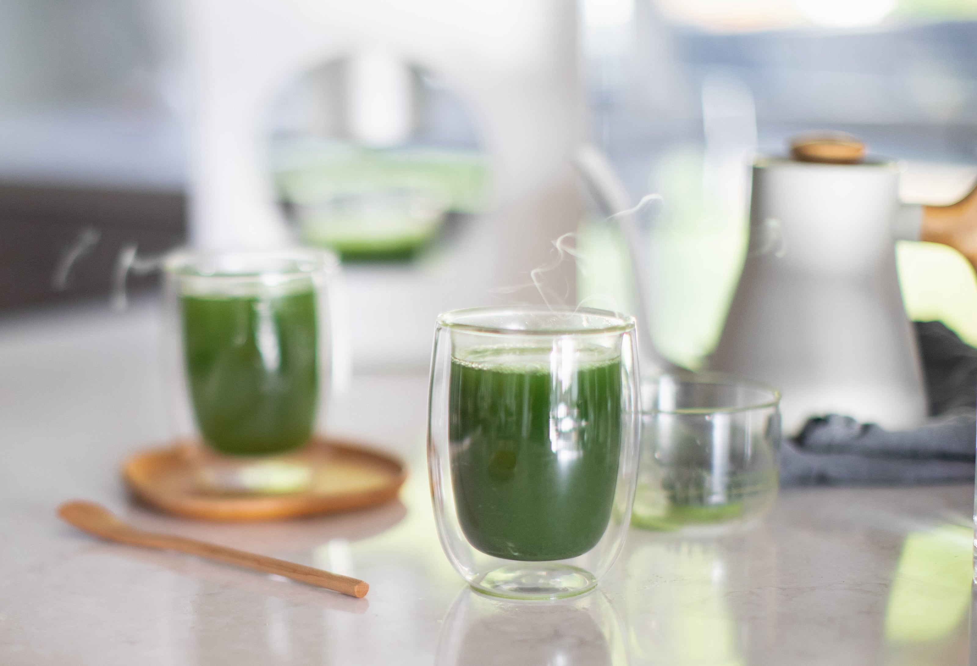 Two steamy glasses of bright green matcha with Cuzen Matcha Maker in the background.