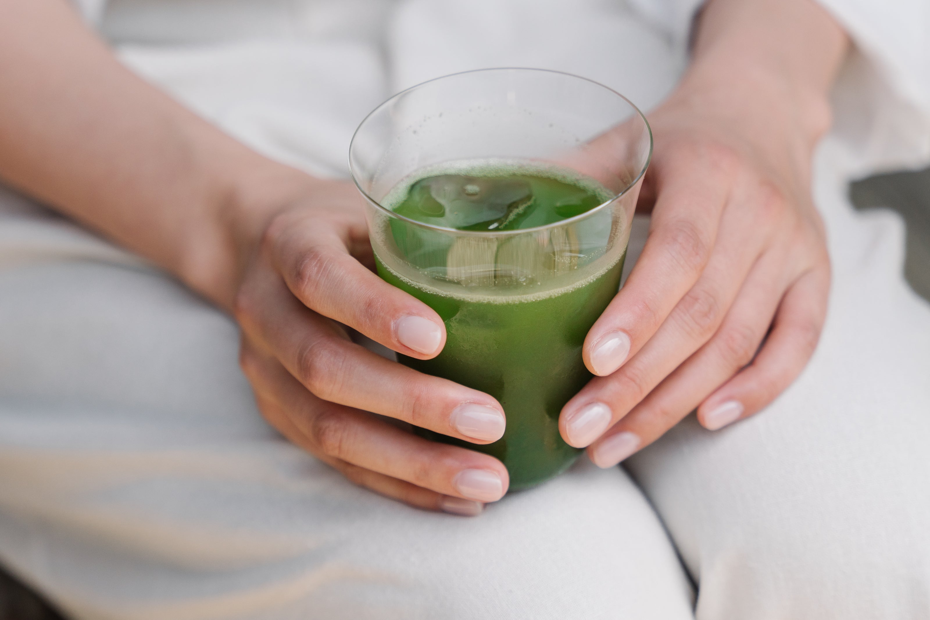 Someone sits, holding a glass of iced matcha on his or her lap.