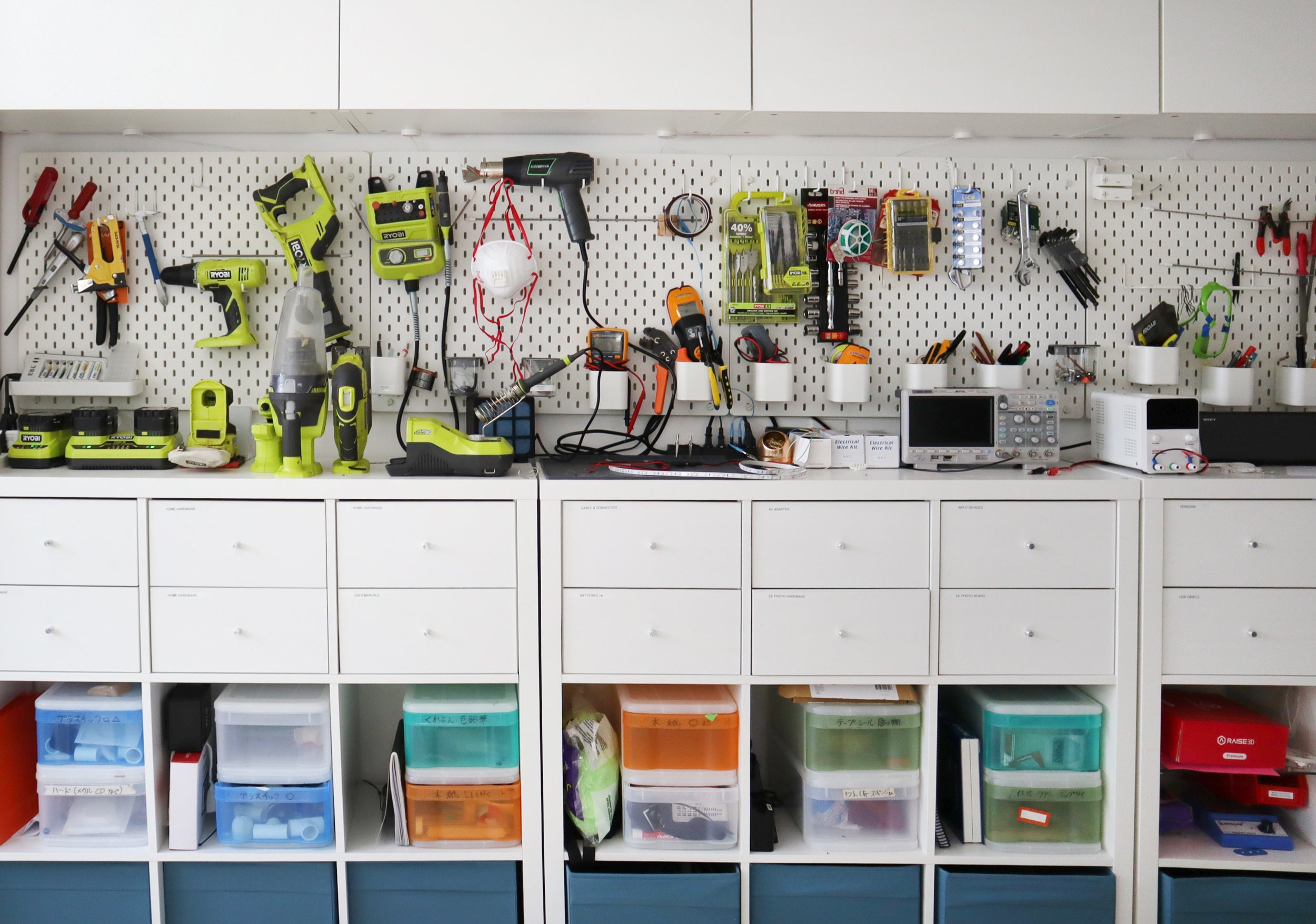  Naoto’s work space features a long white pegboard with brightly-colored tools and gadgets, hanging above rows of drawers and colorful organizing bins. 