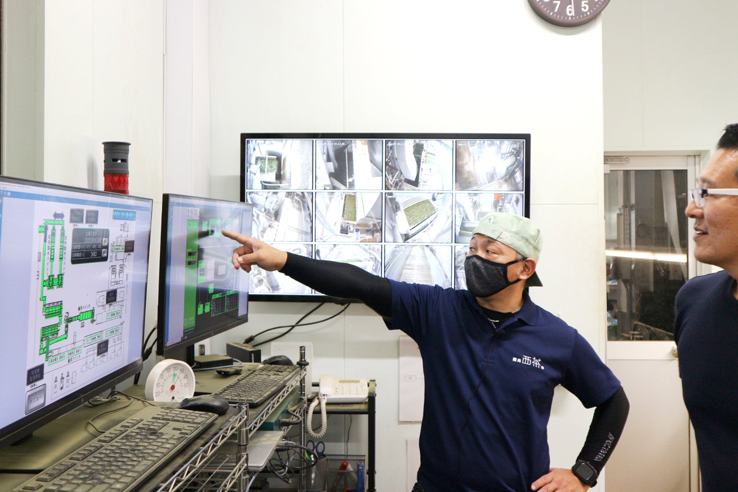 A worker shows Cuzen CEO Eijiro Tsukada how factory conditions are meticulously managed with control room computers.