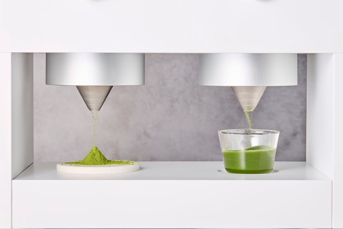 Two Matcha Maker Pro funnels One drops matcha powder while the other whisks a matcha shot.