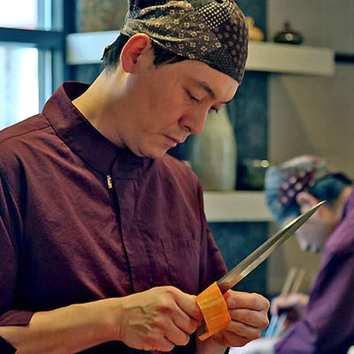 Sushi Taro owner and chef, Nobu Yamazaki, prepares a vegetable with a long knife.