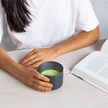 A person sits with a book and a Daily Matcha Bowl full of warm matcha.