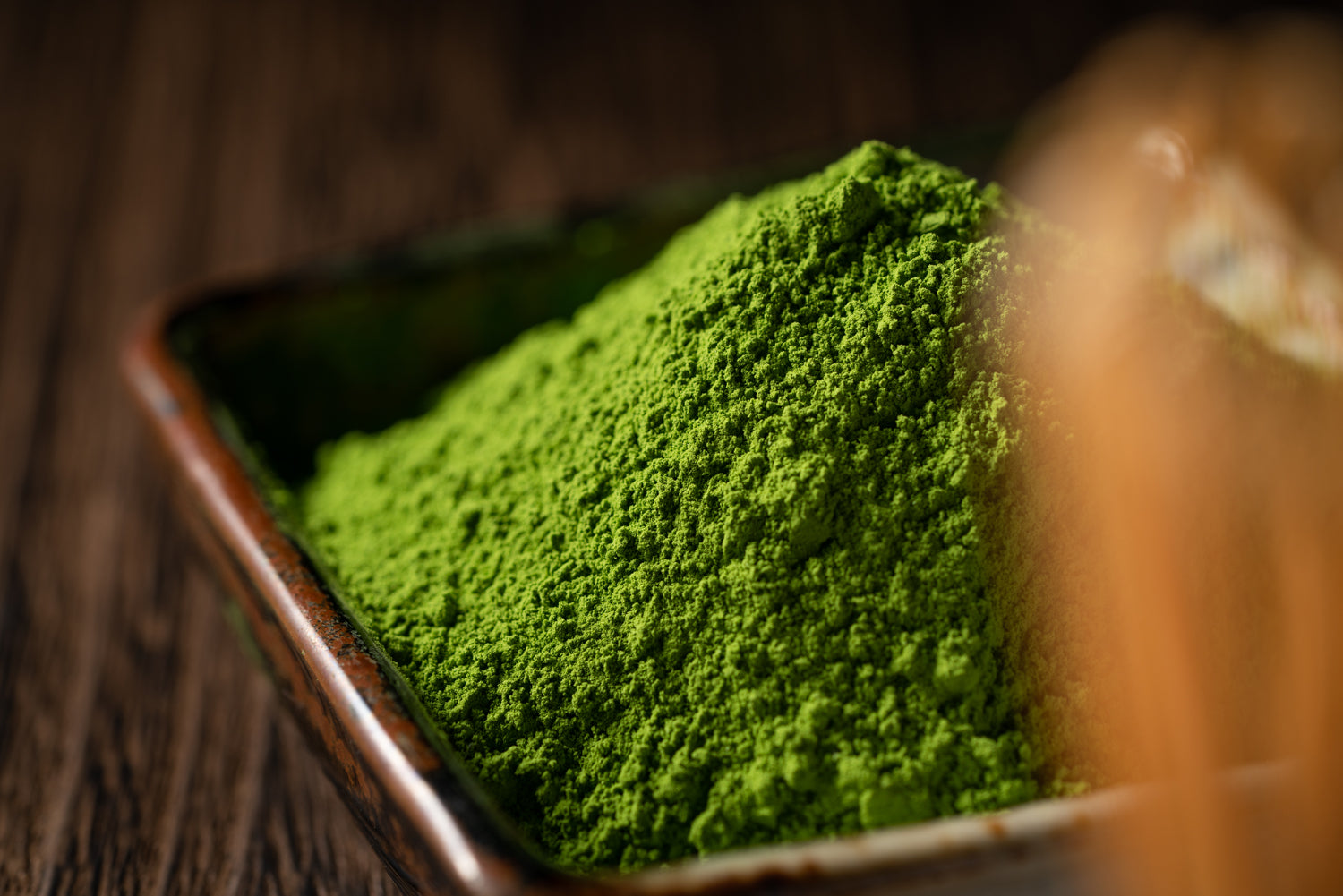 Bright green matcha powder piles high in a rustic-looking tea container.