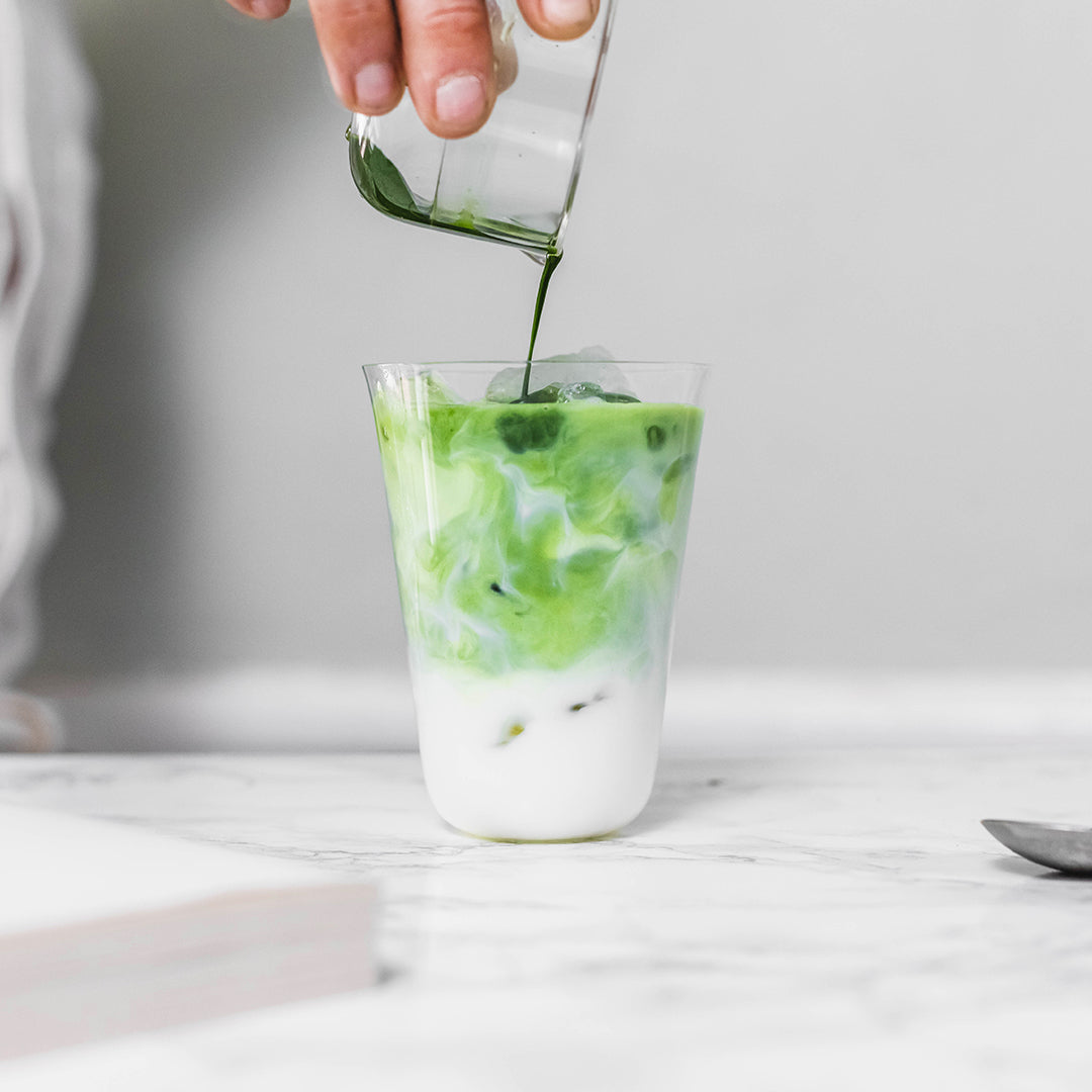 Matcha shot is being poured into a glass of milk.
