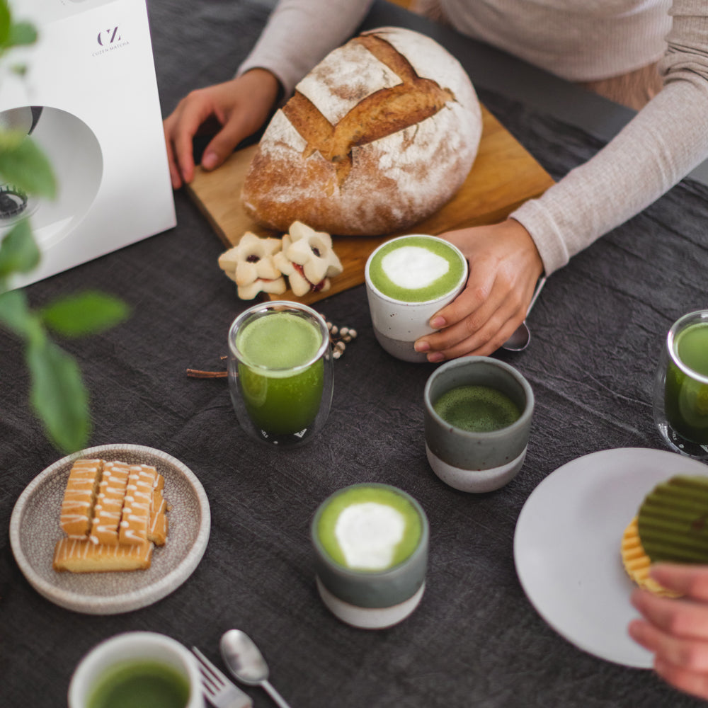 An array of matcha drinks in glasses and ceramic cups on a holiday table, interspersed with holiday pastries.