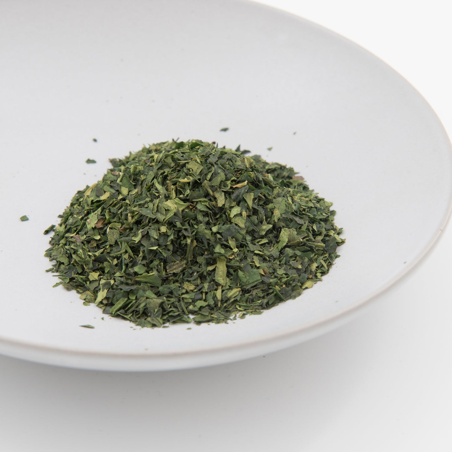  A neat mound of dark green whole matcha leaf on a white plate.